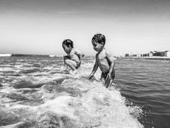 Side view of two boys jumping wave in sea