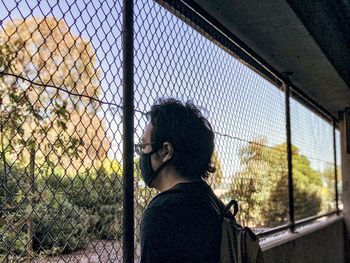 Rear view of man standing by chainlink fence