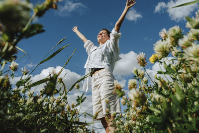 Carefree woman amidst wildflowers standing under sky