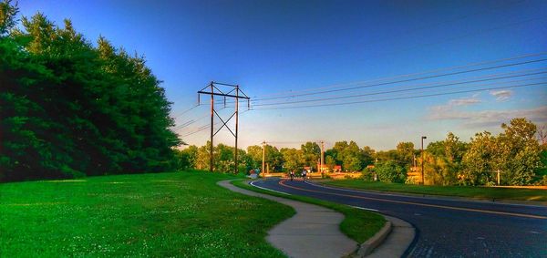 Road by trees against clear blue sky