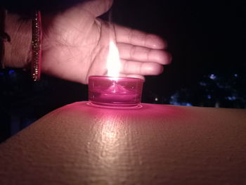 Close-up of hand holding illuminated candle