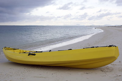 Yellow boat moored at beach against sky