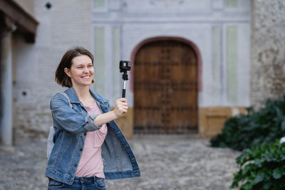 Woman photographing while standing by building