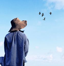 Rear view of woman looking at birds flying in blue sky