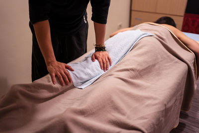 Crop unrecognizable masseur putting white towel on leg of client covered with blanket while doing rehabilitation massage in professional salon