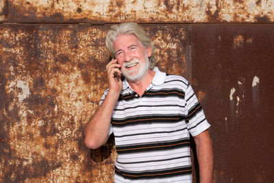 Portrait of smiling man talking over smart phone against wall