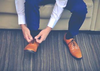 Low section of man tying shoelace while sitting on sofa