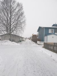 Snow covered road by buildings against sky