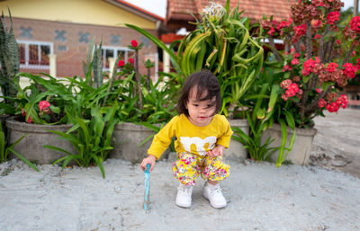 Cute baby girl crouching on footpath against potted plants