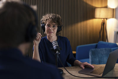 Radio dj wearing eyeglasses and headset interviewing guest in recording studio