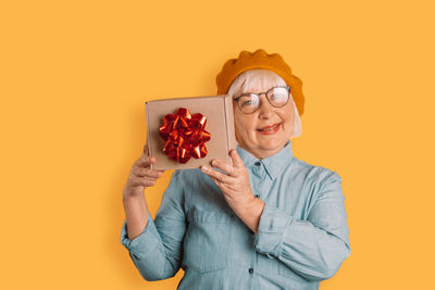 Portrait of young woman holding gift against yellow background