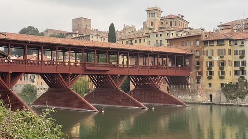 Bridge over river by buildings in city against sky