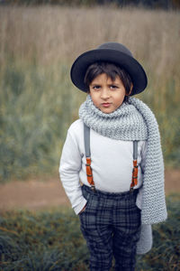 Boy child in plaid pants, hat, suspenders and scarf stands in a field in autumn
