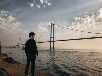 Man standing on bridge over sea against sky