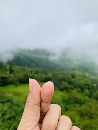 Cropped image of person gesturing against cloudy sky