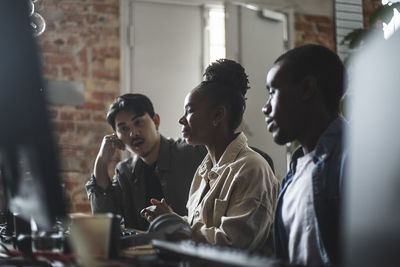 Female hacker discussing with male colleague over computer in creative office