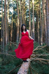 Full length of woman wearing red dress standing on fallen tree in forest