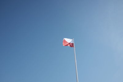 Low angle view of polish flag waving against clear blue sky