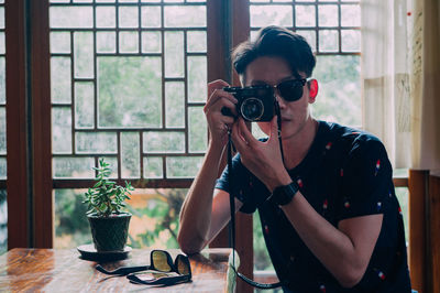 Portrait of woman photographing through window at home