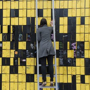 Rear view of woman writing on wall while standing over ladder