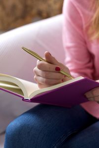 Midsection of woman writing in book at home