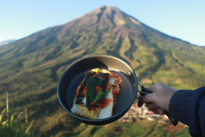 Midsection of person holding ice cream against mountains