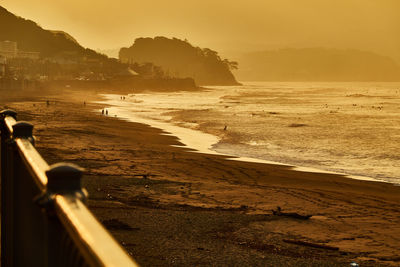 Scenic view of beach with silhouette people against orange sky during sunrise