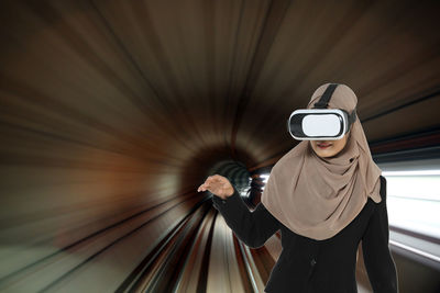 Woman wearing virtual reality simulator while gesturing on railroad track