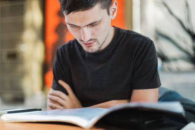 A young man looks through a book menu in a restaurant.
