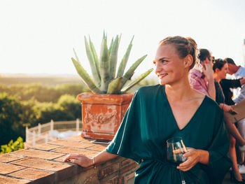 Woman holding wineglass while standing by retaining wall