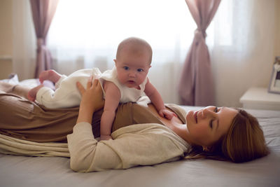 Young mother with red hair is lying on the bed with her daughter at home in the morning