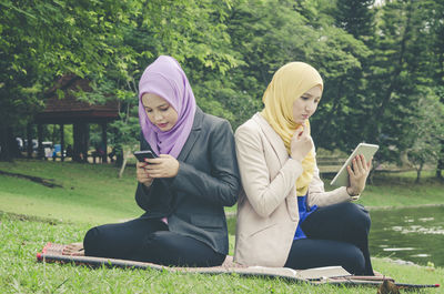 Female friends wearing hijab using technologies at park