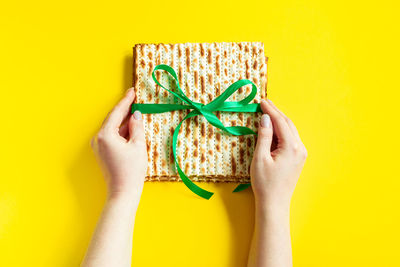 Cropped hands of woman holding gift against yellow background