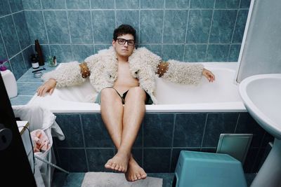 Portrait of young man wearing warm clothes while sitting in bathtub