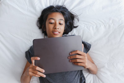 High angle view of girl using digital tablet while lying on bed