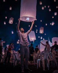 Low angle view of people with paper lanterns at night