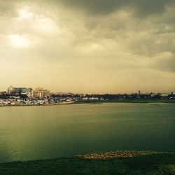 Scenic view of river by cityscape against sky