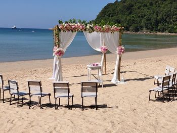 Chairs and tables on beach by sea against sky