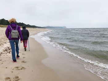 Rear view of women walking on beach against sky