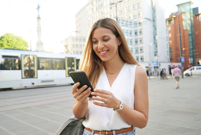 Surprised business woman watching and texting on mobile phone walking in city street