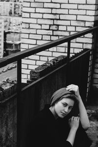 High angle portrait of young woman sitting by weathered wall