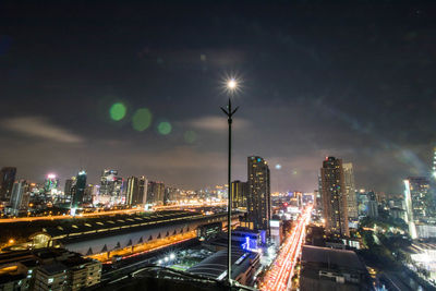 Illuminated street amidst buildings against sky at night