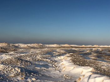 Aerial view of snow covered landscape against clear blue sky