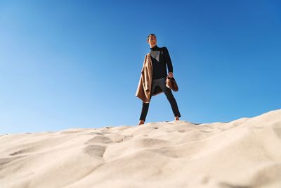 Low angle view of man standing on sand against clear sky