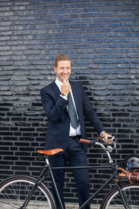 Portrait of happy businessman talking on mobile phone while standing on sidewalk with bicycle