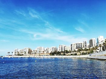 Sea by buildings against blue sky