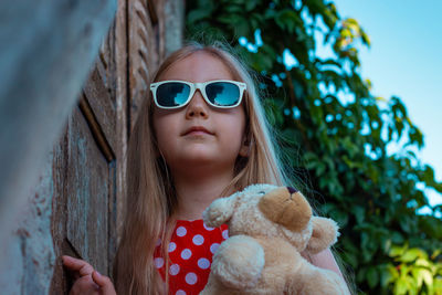 Beautiful happy girl in red polka dot dress soft toy on wooden balcony. cute joyful child long hair.