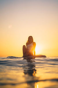 Man sitting in sea against sky during sunset