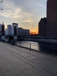 Footpath by buildings against sky during sunset