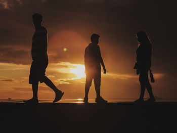 Silhouette people standing on beach against sky during sunset